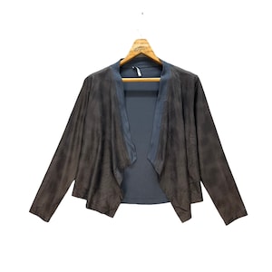 May include: A brown open-front jacket with long sleeves, hanging on a wooden hanger. The jacket has a dark gray interior and a contrasting gray trim along the collar and lapels. The fabric has a textured appearance.
