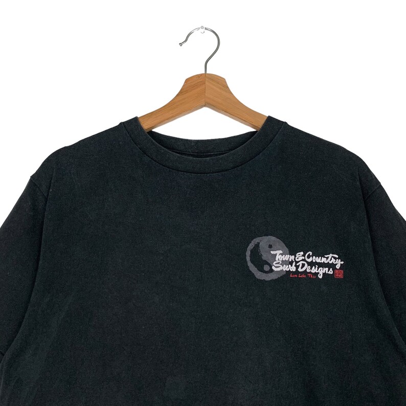 May include: Black t-shirt with a white yin yang symbol and the text "Town & Country Surf Designs" in white with a red stamp.