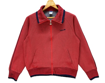 May include: Red zip-up track jacket with blue trim and a small Adidas logo on the chest.