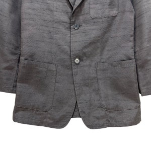Puede incluir: Una chaqueta gris oscura con dos bolsillos de solapa y cierre de bot&oacute;n. La chaqueta tiene una tela texturizada.