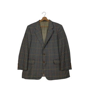 May include: A plaid blazer in shades of brown, blue, and orange, hanging on a wooden hanger. The blazer has two front pockets and brown buttons. The interior lining is a light tan color.
