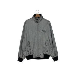 Peut inclure: Veste grise avec col, poignets et ourlet noirs. La veste a une fermeture éclair, deux poches avant et un petit logo sur la poitrine. Fabriquée dans un matériau léger.