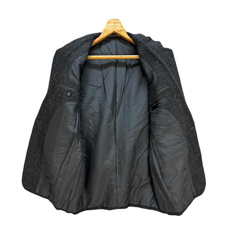 Puede incluir: Una chaqueta de lana gris con forro negro. La chaqueta tiene un cierre de bot&oacute;n &uacute;nico y dos bolsillos en la parte delantera.