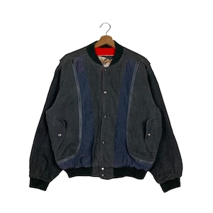 Puede incluir: Una chaqueta bomber de mezclilla negra con paneles azules y grises y un forro rojo. La chaqueta tiene una cremallera y dos bolsillos.
