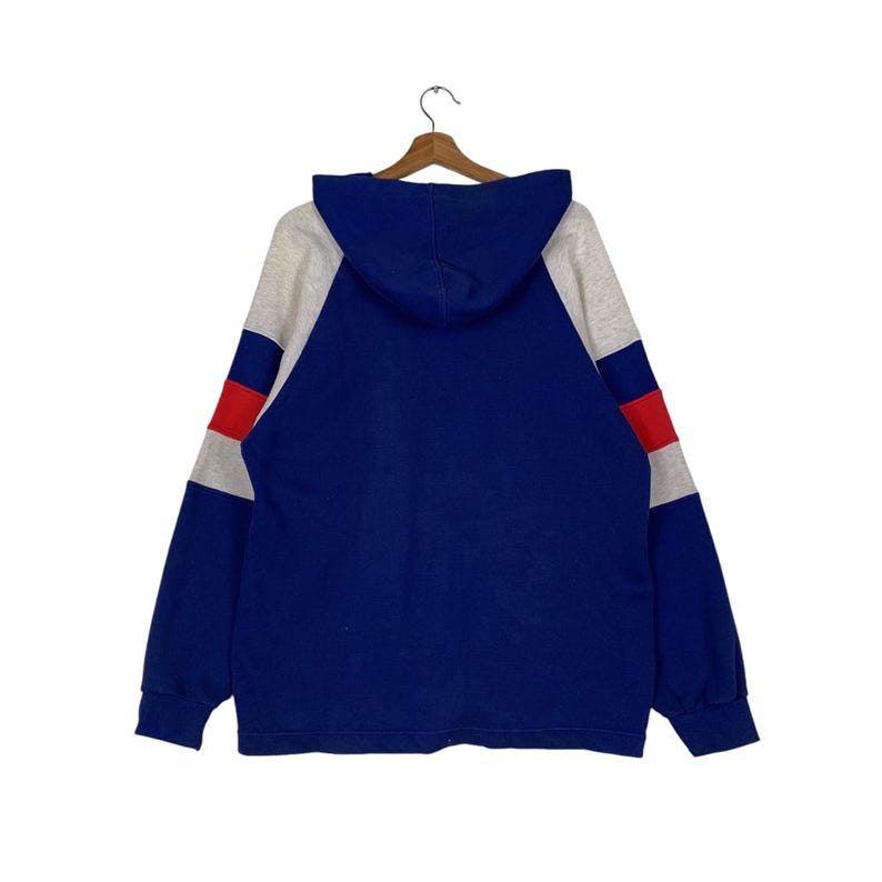 Puede incluir: Una sudadera con capucha azul con mangas grises y blancas y rayas rojas y blancas en las mangas.