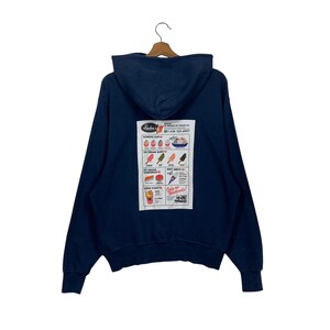 Op de afbeelding: Een marineblauw hoodie met een vintage reclame voor een ijssalon op de achterkant. De reclame toont een menu met verschillende ijsopties, waaronder sundaes, ijsstokjes, ijs-sandwiches, softijs en sodafloat. De tekst op de reclame luidt "Rader's", "Sundaes Cups", "Ice Cream Bars", "Ice Cream Sandwiches", "Soft Serve", "Soda Floats", en "Come on Down!"