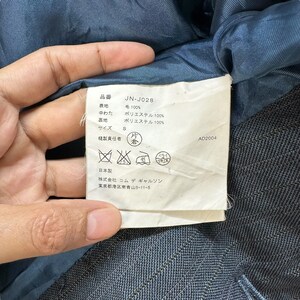 Puede incluir: Una etiqueta blanca con texto negro que detalla la composici&oacute;n de una prenda. La etiqueta dice "品番 JN-J028 表地 毛 100% 中わた ポリエステル 100% 裏地 ポリエステル 100% サイズ S 縫製責任者 片 倉 日本製 株式会社 コムデギャルソン 東京都港区南青山5-11-5 AD2004".