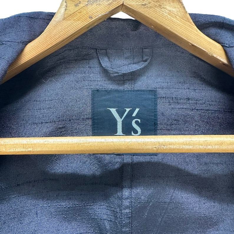 Puede incluir: Una chaqueta azul oscuro con una etiqueta negra que dice "Y's" en la parte posterior.