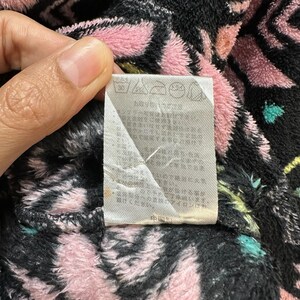 May include: A white care label with black text and symbols. The label has instructions for washing, drying, and ironing the garment. The label is attached to a black and pink patterned fabric.