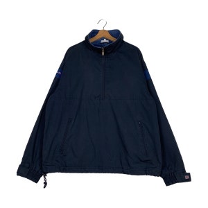 Op de afbeelding: Een donkerblauw, lang mouwig, met rits te sluiten jack met een hoge kraag. Het jack heeft twee zakken aan de voorkant en een klein logo op de mouw.