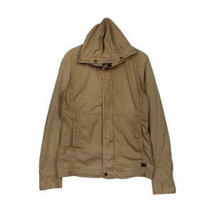 May include: A tan hooded jacket with a button-up front and two front pockets. The jacket has a drawstring hood and a small logo patch near the bottom hem. The jacket is made of a durable, lightweight fabric.