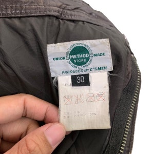 May include: A green label with the text "Established 1995 Produced 8888 Method Store Union Men S3 0000  Method Made  Produced by C's Men" and a black label with the text "Style 30". The label has care instructions in Japanese and the text "牛革" and "ナイロン 100%".