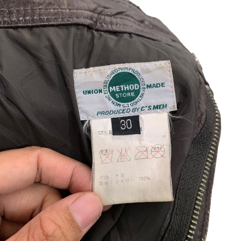 May include: A green label with the text "Established 1995 Produced 8888 Method Store Union Men S3 0000  Method Made  Produced by C's Men" and a black label with the text "Style 30". The label has care instructions in Japanese and the text "牛革" and "ナイロン 100%".