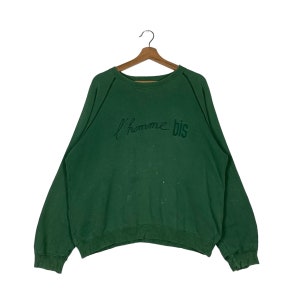Puede incluir: Sudadera verde con cuello redondo y mangas largas. La sudadera tiene el texto "l'homme bis" bordado en la parte delantera en color verde oscuro.