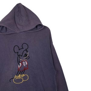 May include: A purple hooded sweatshirt with a black and white outline of Mickey Mouse wearing red shorts. The outline of Mickey Mouse is filled in with red and yellow.