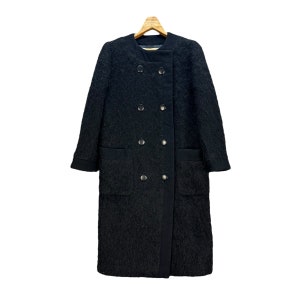 May include: A black, textured coat with a double-breasted design. The coat features two rows of silver buttons, two front pockets, and a notched collar. The coat is hanging on a wooden hanger.