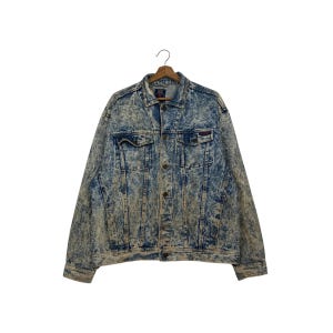 Peut inclure: Veste en jean délavée à l'acide avec un col classique, une fermeture boutonnée sur le devant et deux poches de poitrine. La veste présente un motif bleu et blanc délavé et est suspendue à un cintre en bois. Veste de style vintage.