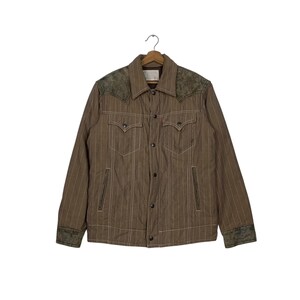 May include: Brown jacket with vertical white stripes, featuring a button-up front, two chest pockets, and two side pockets. The jacket has a collar and decorative stitching. The shoulders and cuffs have a textured, darker green fabric.