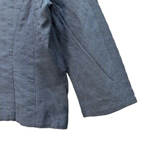 Puede incluir: Una chaqueta azul con un patr&oacute;n de rayas finas. La chaqueta tiene un cierre de un bot&oacute;n y mangas largas.
