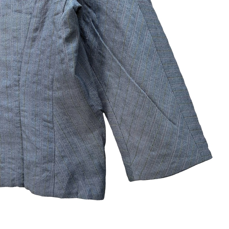 Puede incluir: Una chaqueta azul con un patr&oacute;n de rayas finas. La chaqueta tiene un cierre de un bot&oacute;n y mangas largas.