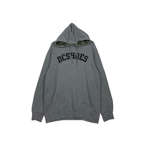 May include: A gray hoodie with the text "DCSHOES" in black across the chest. The hood lining features a camouflage pattern. The hoodie has a front pocket and ribbed cuffs and hem.