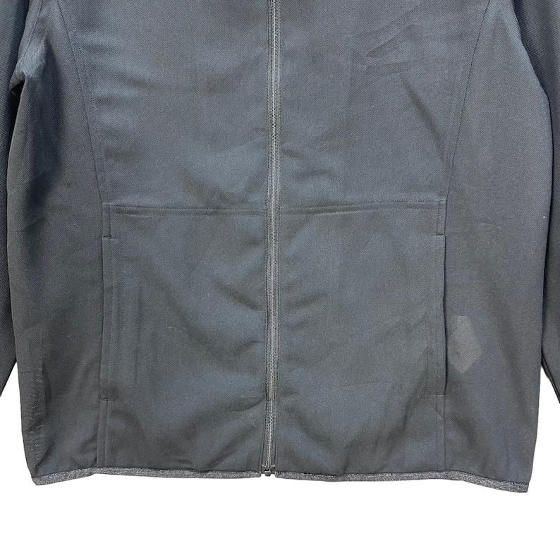 May include: A black zippered jacket with a pocket on the left side. The jacket has a ribbed hem and cuffs.