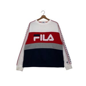May include: A color-block Fila sweatshirt in white, red, gray, and navy blue. The word "FILA" is prominently displayed in white block letters across the chest. The sleeves have a red stripe with the Fila logo.