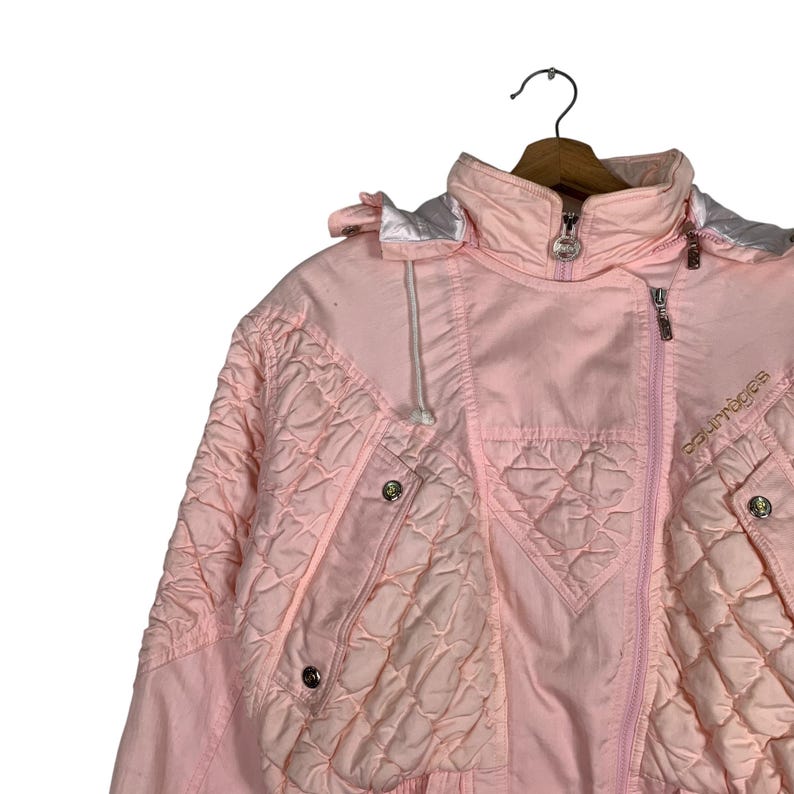 May include: A pink quilted ski jacket with a white hood and a zip closure. The jacket has a logo that says "doublouger" on the right side.