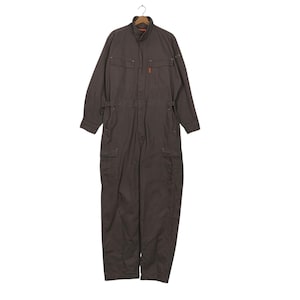 Puede incluir: Un mono de trabajo marrón con mangas largas, cuello y múltiples bolsillos. El mono tiene cierre de cremallera y cinturón en la cintura. La prenda está colgada de una percha de madera.