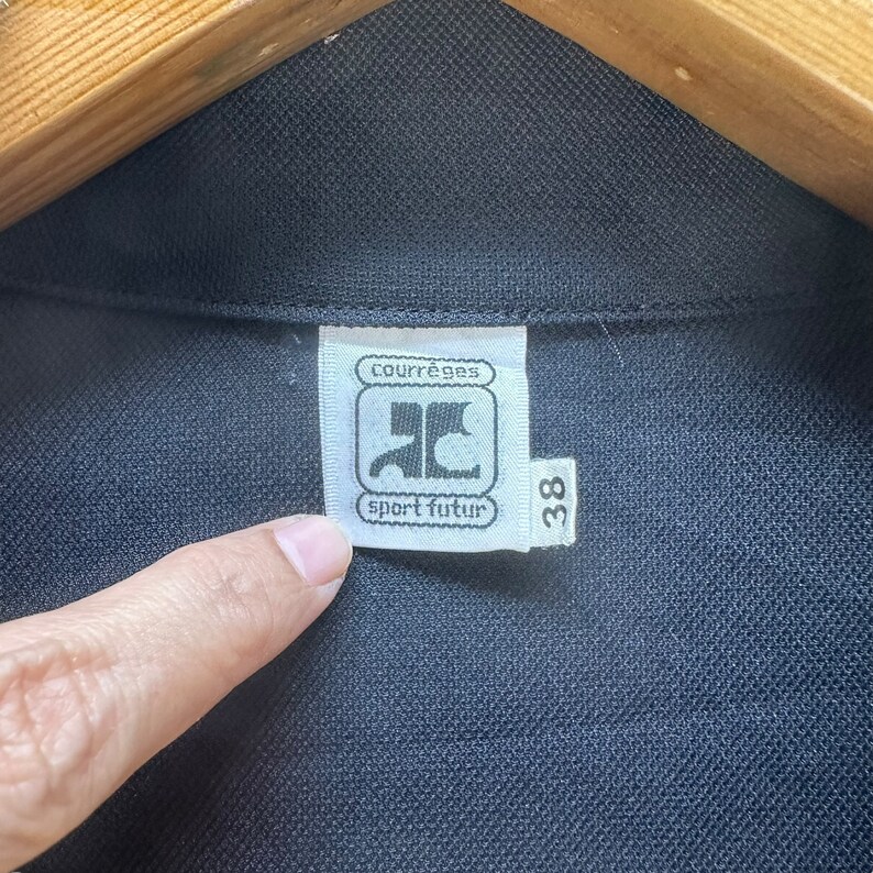May include: A black and white label with the text "Courr&egrave;ges sport futur" and a logo of a stylized "C" with a bird inside. The label also has the number "38" printed on it.