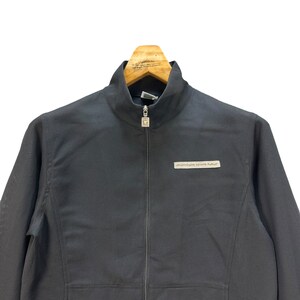May include: A black zip-up jacket with a stand-up collar and a small logo that says "courr&egrave;ges sport futur" on the left chest.