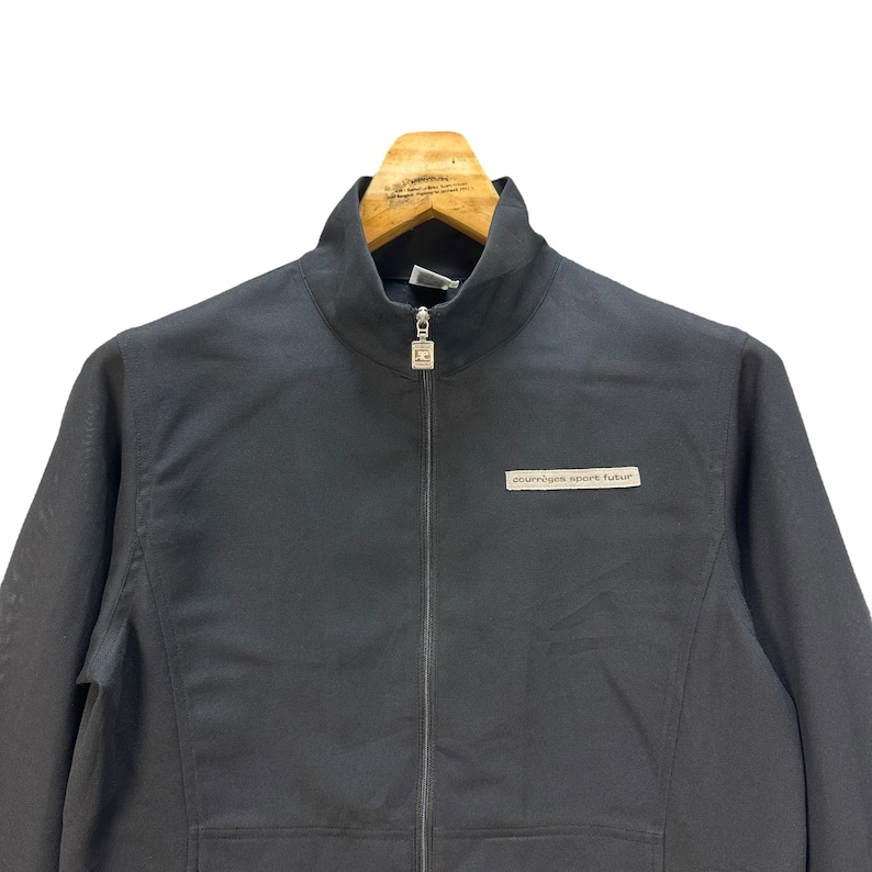 May include: A black zip-up jacket with a stand-up collar and a small logo that says "courr&egrave;ges sport futur" on the left chest.