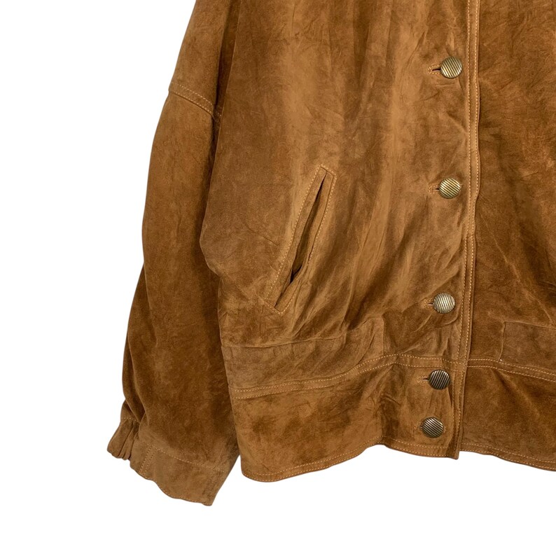May include: A brown suede jacket with a button-up front and two pockets. The jacket has a classic design with a soft, textured appearance. The buttons are a gold color.