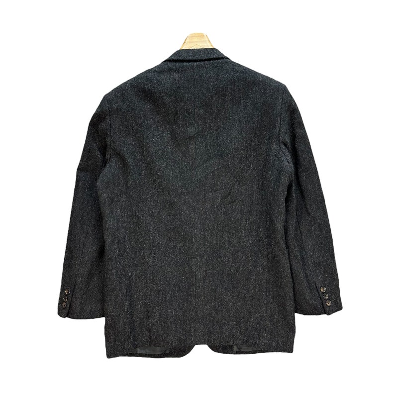 Puede incluir: Una chaqueta de tweed gris oscuro con cierre de un bot&oacute;n. La chaqueta tiene un corte cl&aacute;sico y una tela ligeramente texturizada.