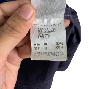 May include: A white care label with black text and symbols. The label includes washing instructions, fabric content, and a style number: STYLE NO.6145117. The text reads: "Hand wash, 30 degrees Celsius, do not bleach, do not tumble dry, iron at medium temperature, do not dry clean.  Fabric content: 100% cotton.  Separate fabric: 100% cotton.  Do not use a tumble dryer.  Close the zipper before washing."