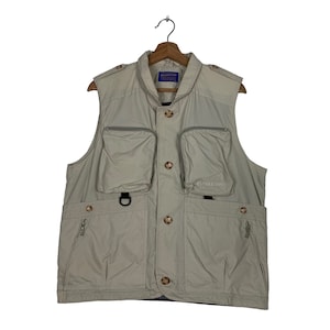 Puede incluir: Un chaleco utilitario beige con múltiples bolsillos y un logotipo de Pendleton en la parte delantera. El chaleco tiene una cremallera y detalles de botones.