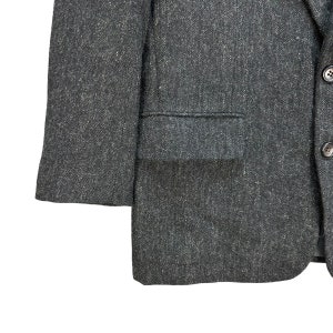 Puede incluir: Una chaqueta de traje gris oscuro con tejido texturizado. La chaqueta tiene un cierre de bot&oacute;n &uacute;nico y un bolsillo de solapa en el lado izquierdo.