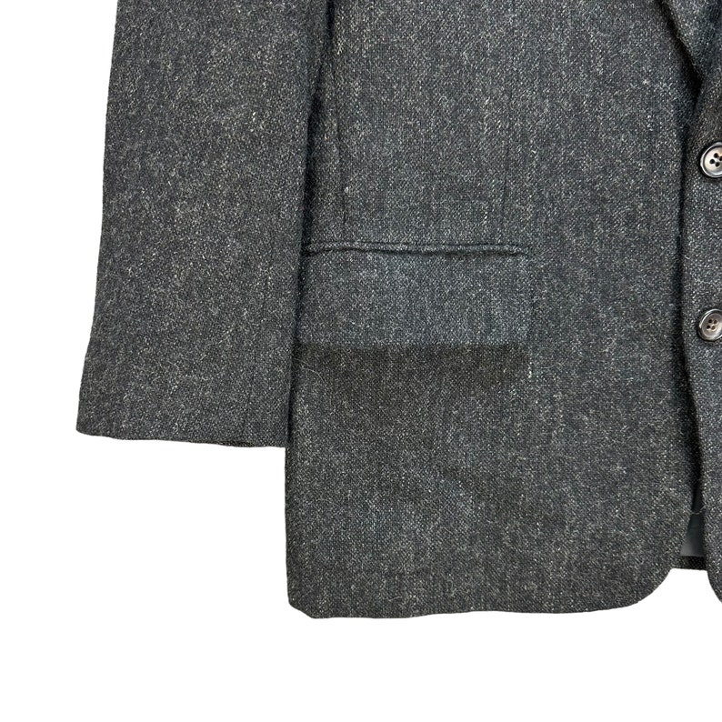 Puede incluir: Una chaqueta de traje gris oscuro con tejido texturizado. La chaqueta tiene un cierre de bot&oacute;n &uacute;nico y un bolsillo de solapa en el lado izquierdo.