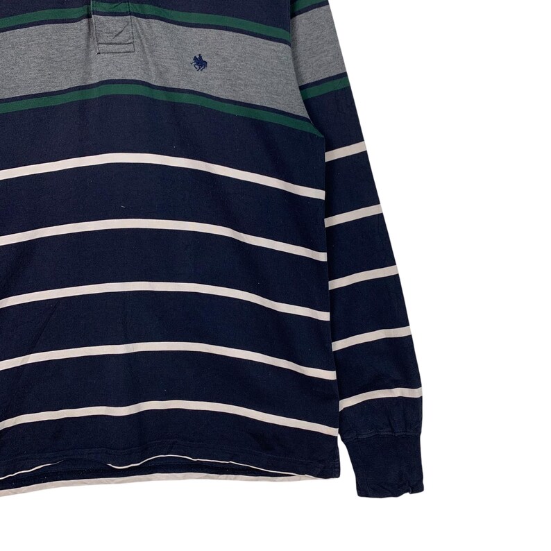 May include: Navy blue long-sleeve shirt with white horizontal stripes. The shirt has a gray and green striped collar and a small embroidered emblem. The sleeves have a ribbed cuff.