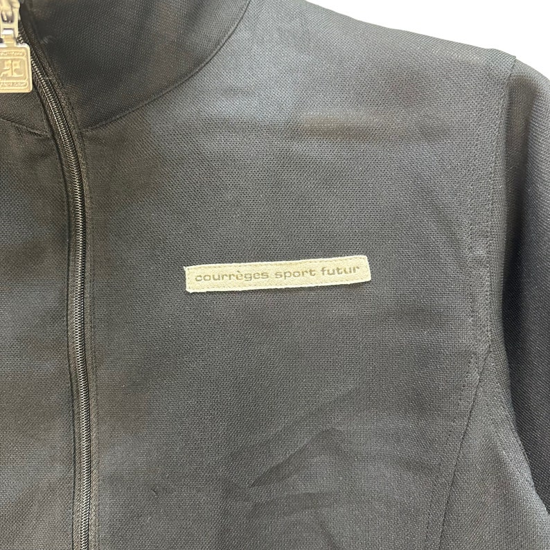 May include: A black zippered jacket with a brown patch that reads "courr&egrave;ges sport futur".