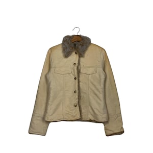 May include: Cream-colored jacket with a faux fur collar. The jacket has a button-up front, two chest pockets, and long sleeves. The jacket is hanging on a wooden hanger against a white background.
