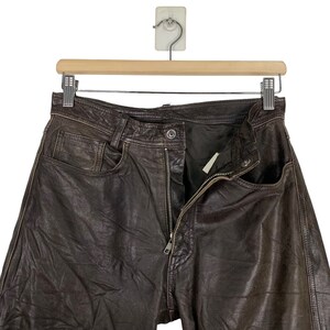 May include: Brown leather pants with a zipper fly and a button closure. The pants have a classic five-pocket design.
