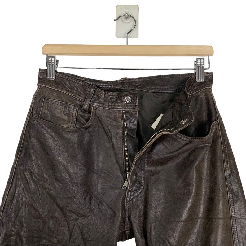 May include: Brown leather pants with a zipper fly and a button closure. The pants have a classic five-pocket design.