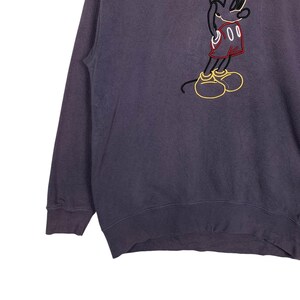 May include: A dark purple sweatshirt with a white outline of Mickey Mouse wearing red shorts and a yellow smile.