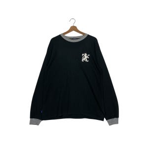 May include: Black long-sleeve shirt with a gray crew neck and cuffs. A white embroidered lion crest is on the left chest. The shirt is hanging on a wooden hanger against a white background.