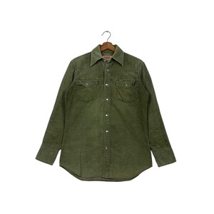 May include: Olive green corduroy shirt with long sleeves, a button-down front, and two chest pockets. The shirt is hanging on a wooden hanger against a white background. The shirt has a classic western style.