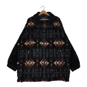 Könnte beinhalten: Schwarze Fleecejacke mit geometrischem Muster in Rot, Weiß und Beige. Die Jacke hat einen Reißverschluss und zwei Taschen. Das Etikett lautet "Pendleton".