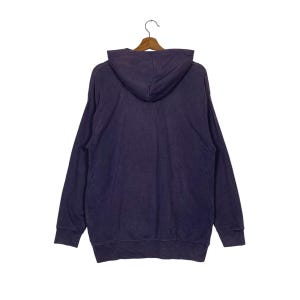 May include: A dark purple hooded sweatshirt with long sleeves and a kangaroo pocket. The sweatshirt is hanging on a wooden hanger.