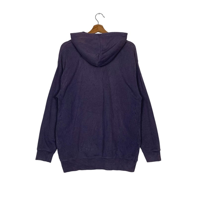 May include: A dark purple hooded sweatshirt with long sleeves and a kangaroo pocket. The sweatshirt is hanging on a wooden hanger.
