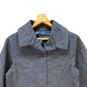 Puede incluir: Una chaqueta gris de rayas finas con cuello y cierre de bot&oacute;n. La chaqueta tiene una etiqueta que dice "JUNYA WATANABE" en el interior del cuello.